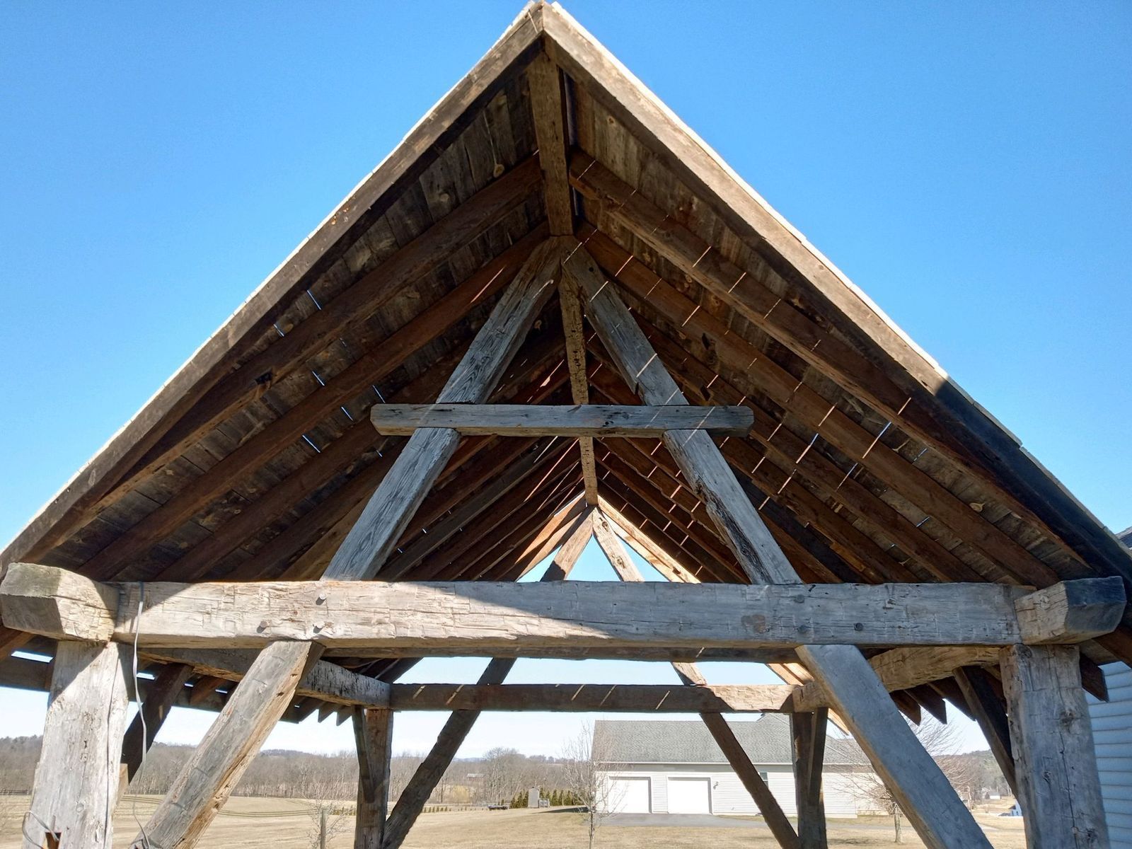 Wooden framing of a peaked roof structure against a clear blue sky, showing exposed beams and rafters.