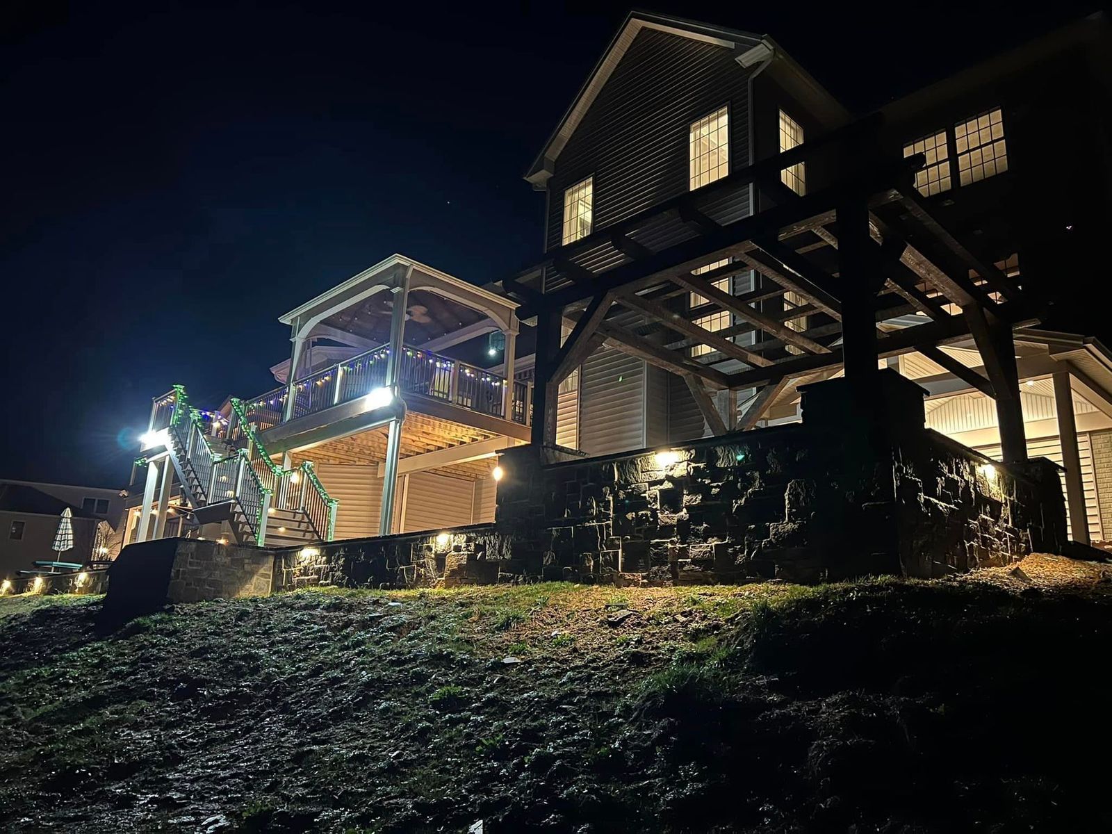 A wooden pergola by Central Timber Frame Supply serving PA, WV, VA, NY, NJ , and stone accents, viewed from a grassy slope.