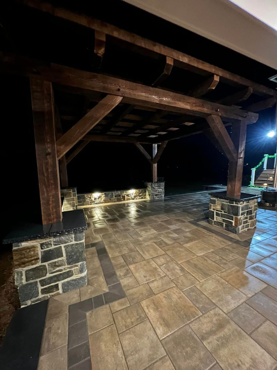 Wooden pergola, stone pillars, and low-level accent lighting. Built by Custom Timber Frame Supply. 