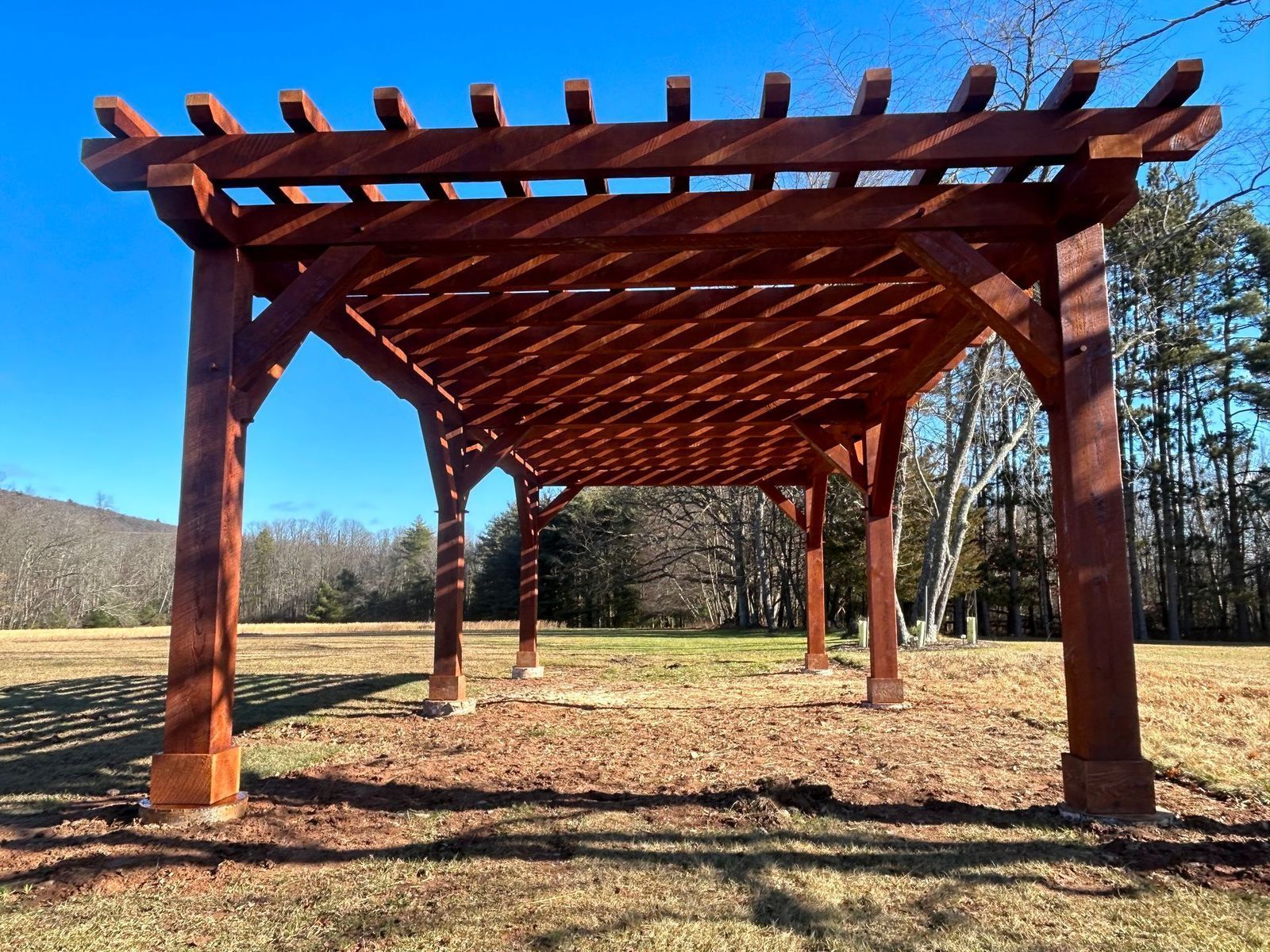 A large, reddish-brown wooden pergola by Central Timber Frame Supply available for wholesale across the United States