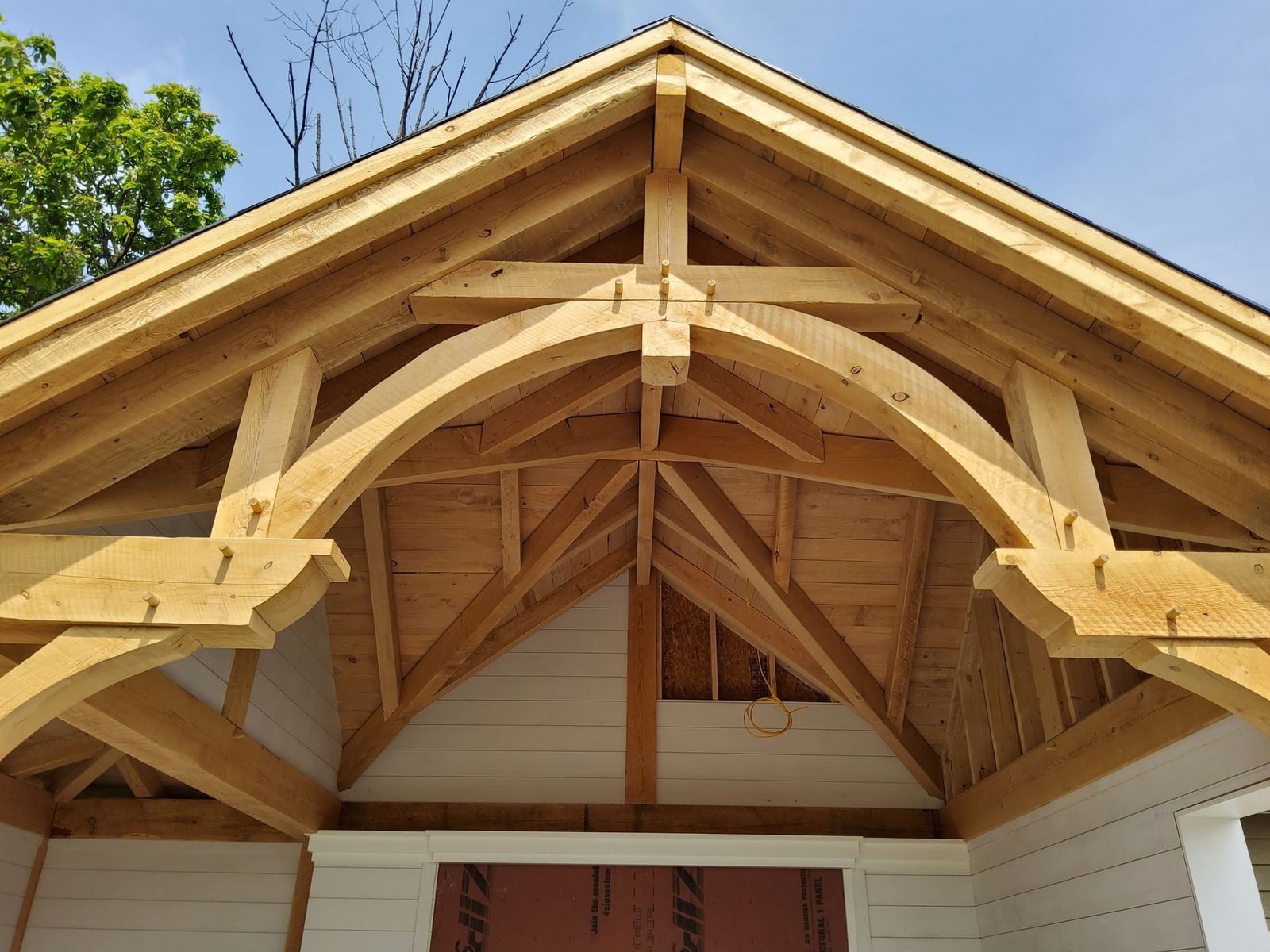 The wooden frame of a porch roof, by Central Timber Frame Supply featuring a decorative curved arch beam