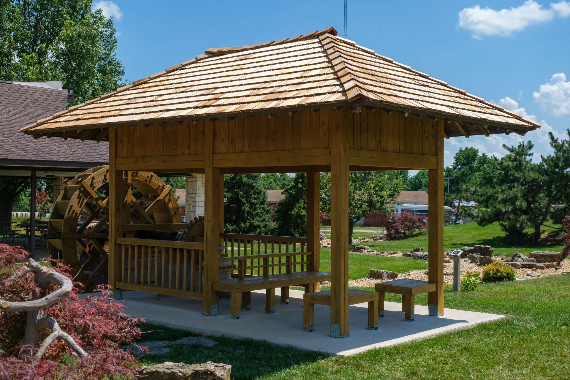 Wooden gazebo with shingled roof in a landscaped garden on a sunny day