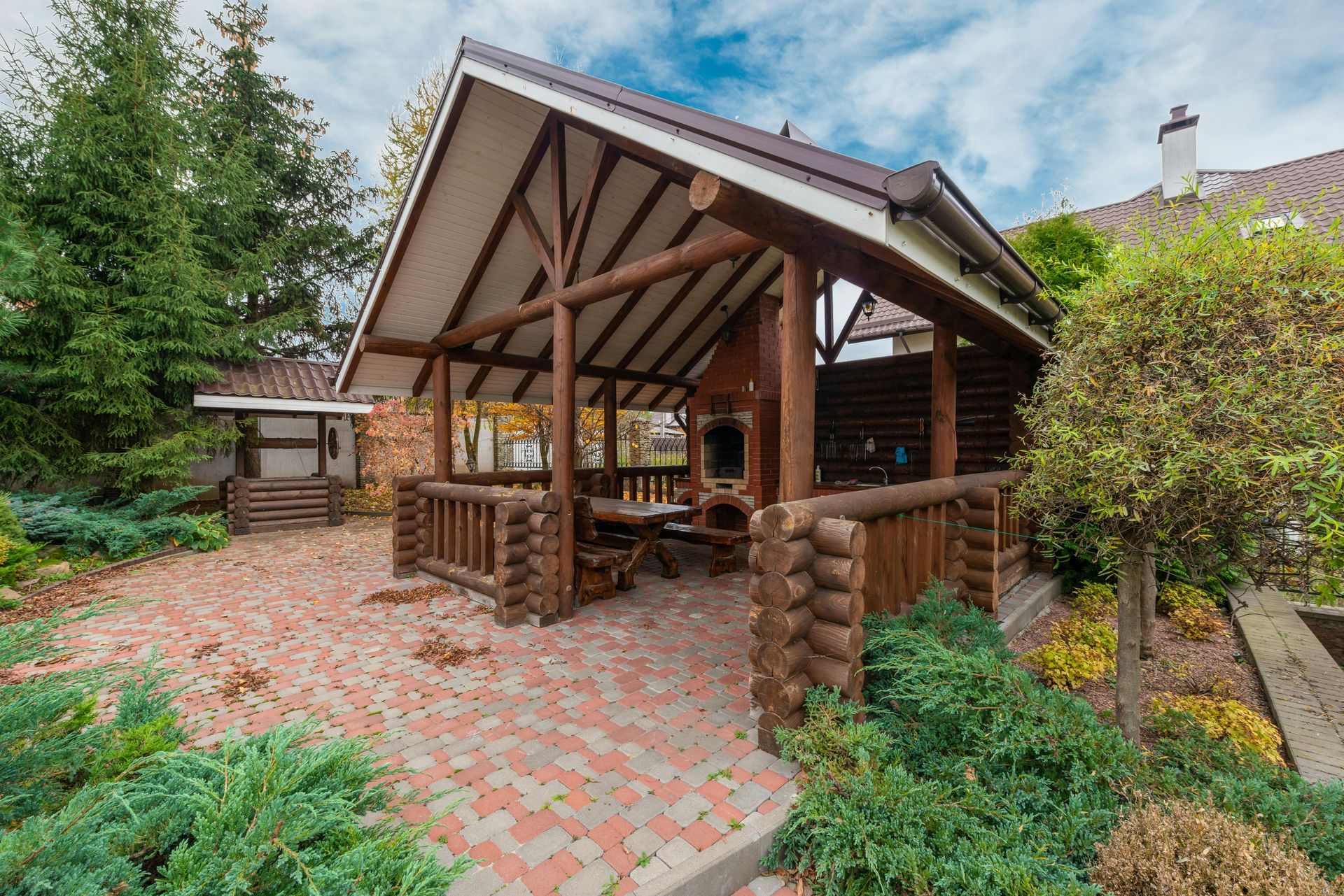 Wooden gazebo pavilion with brick patio and surrounding greenery in a landscaped backyard