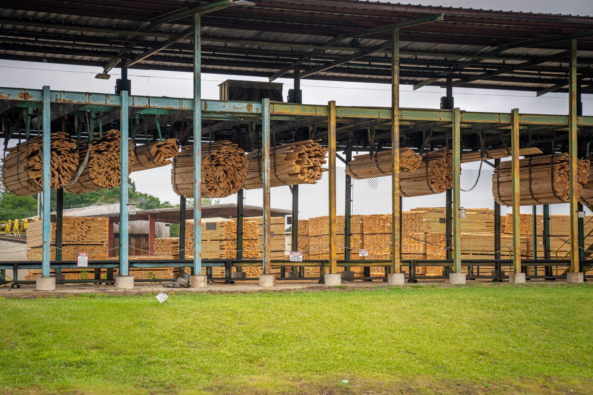 Outdoor shelter with stacked logs under a metal roof beside a grassy field