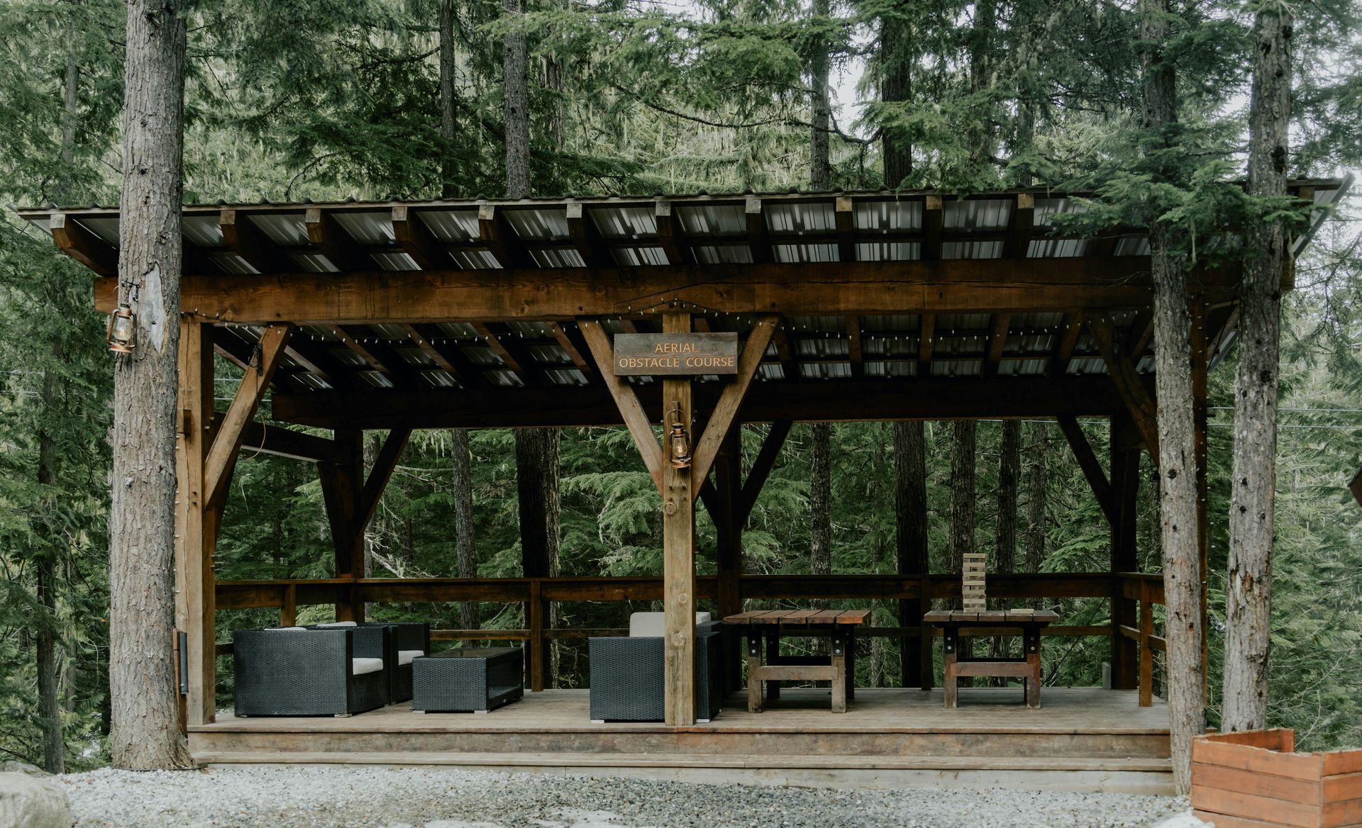 Open-air wooden pavilion in a forest, with lounge chairs and a stone floor.