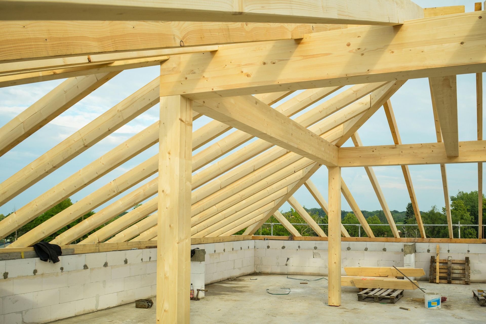 Wooden roof trusses under construction atop concrete block walls on a building site