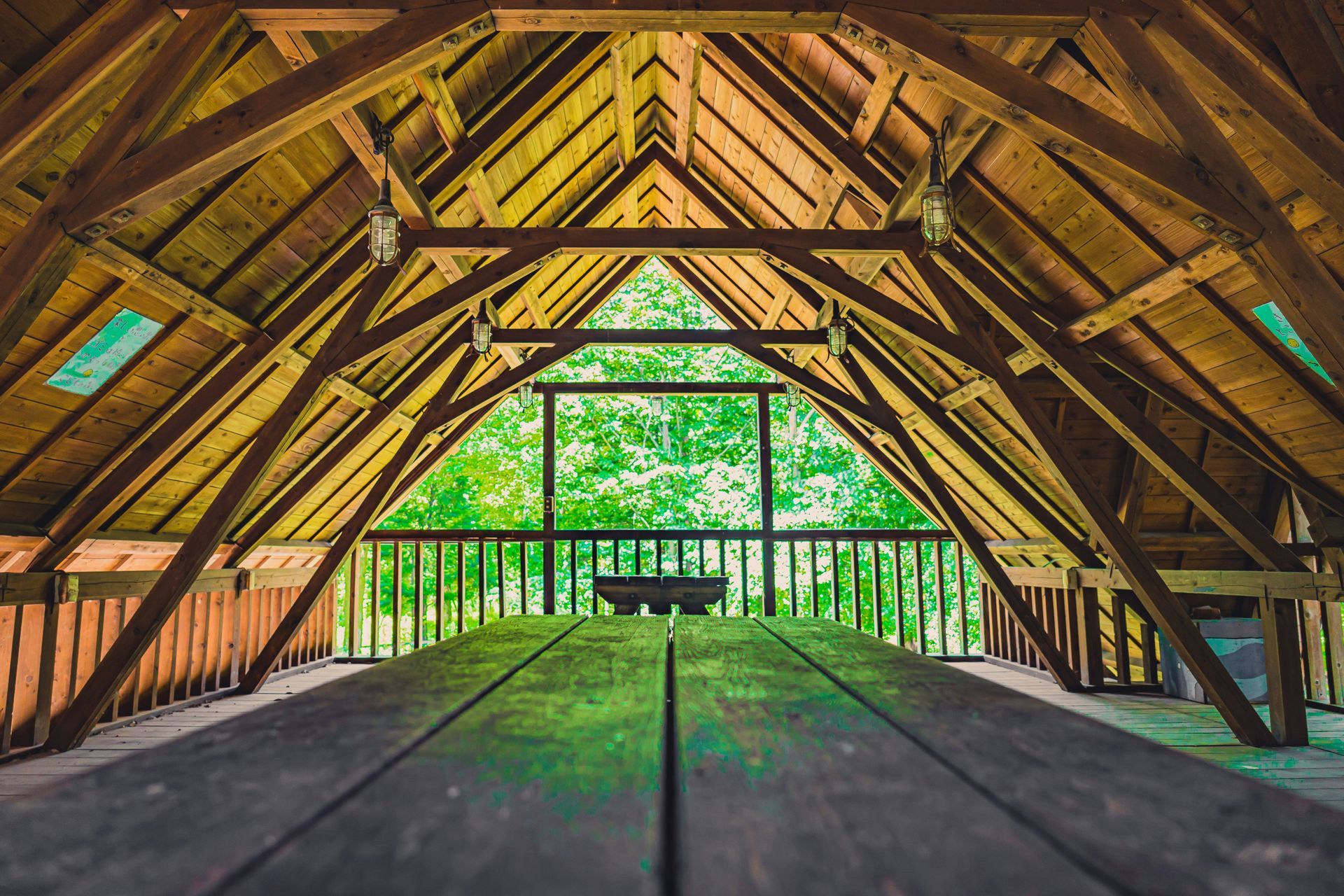 Wooden attic loft with exposed beams, open railing, and bright green trees visible through the far opening
