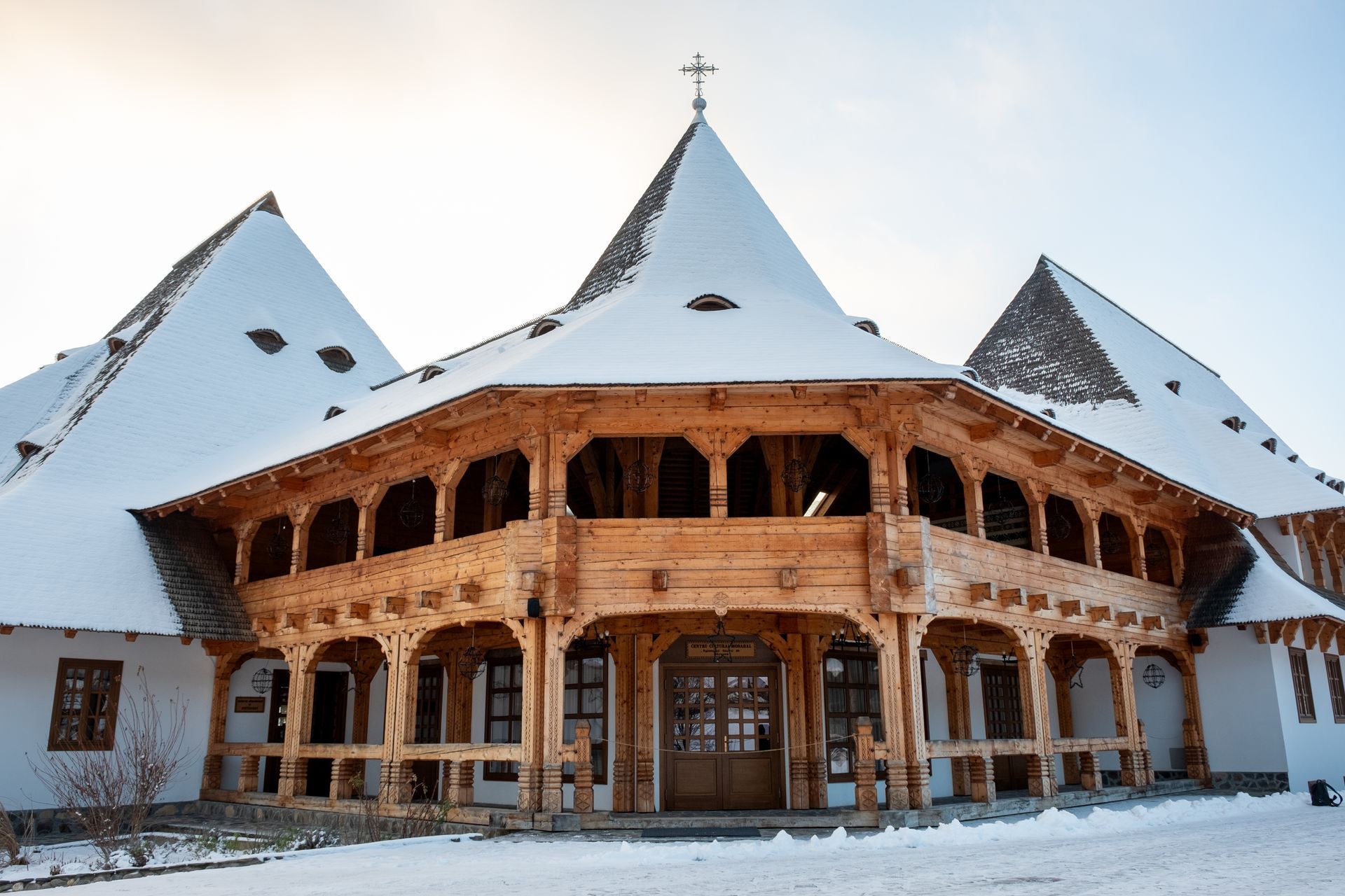 Snow-covered wooden chalet with steep white roofs and a central carved balcony in a winter setting