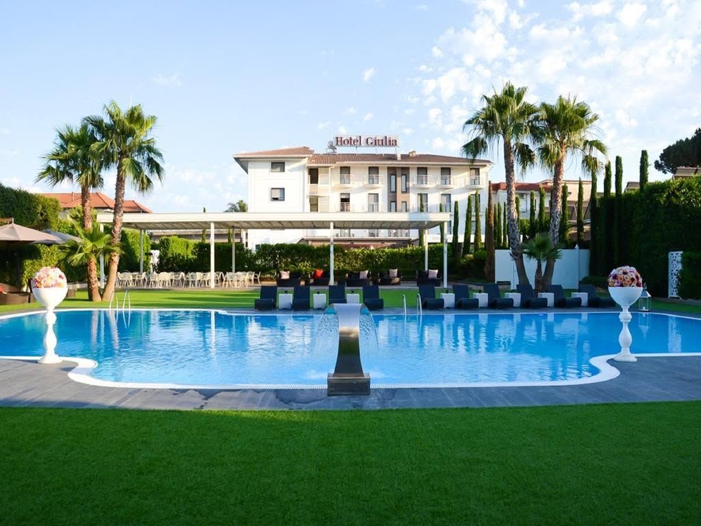 Piscina del resort con acqua azzurra, palme, lettini e un edificio alberghiero sullo sfondo.