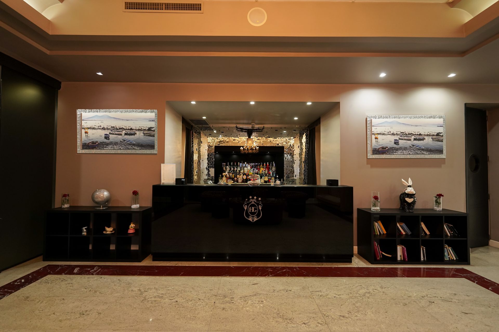 Bancone della reception nella hall dell'hotel con piano in legno scuro, illuminazione calda e decorazioni simmetriche.