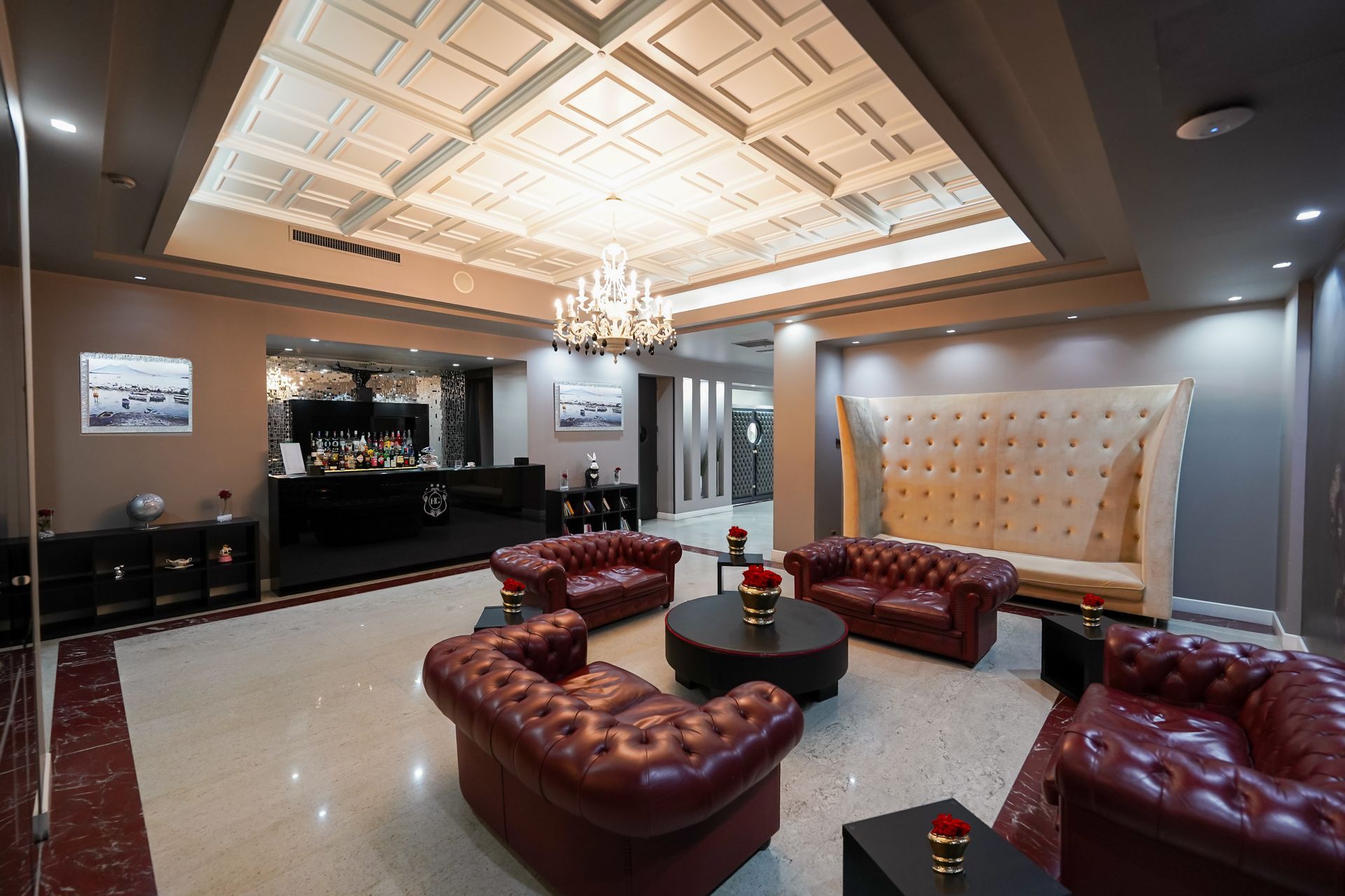 Elegante hall d'albergo con divani in pelle rossa, lampadario e soffitto decorato.