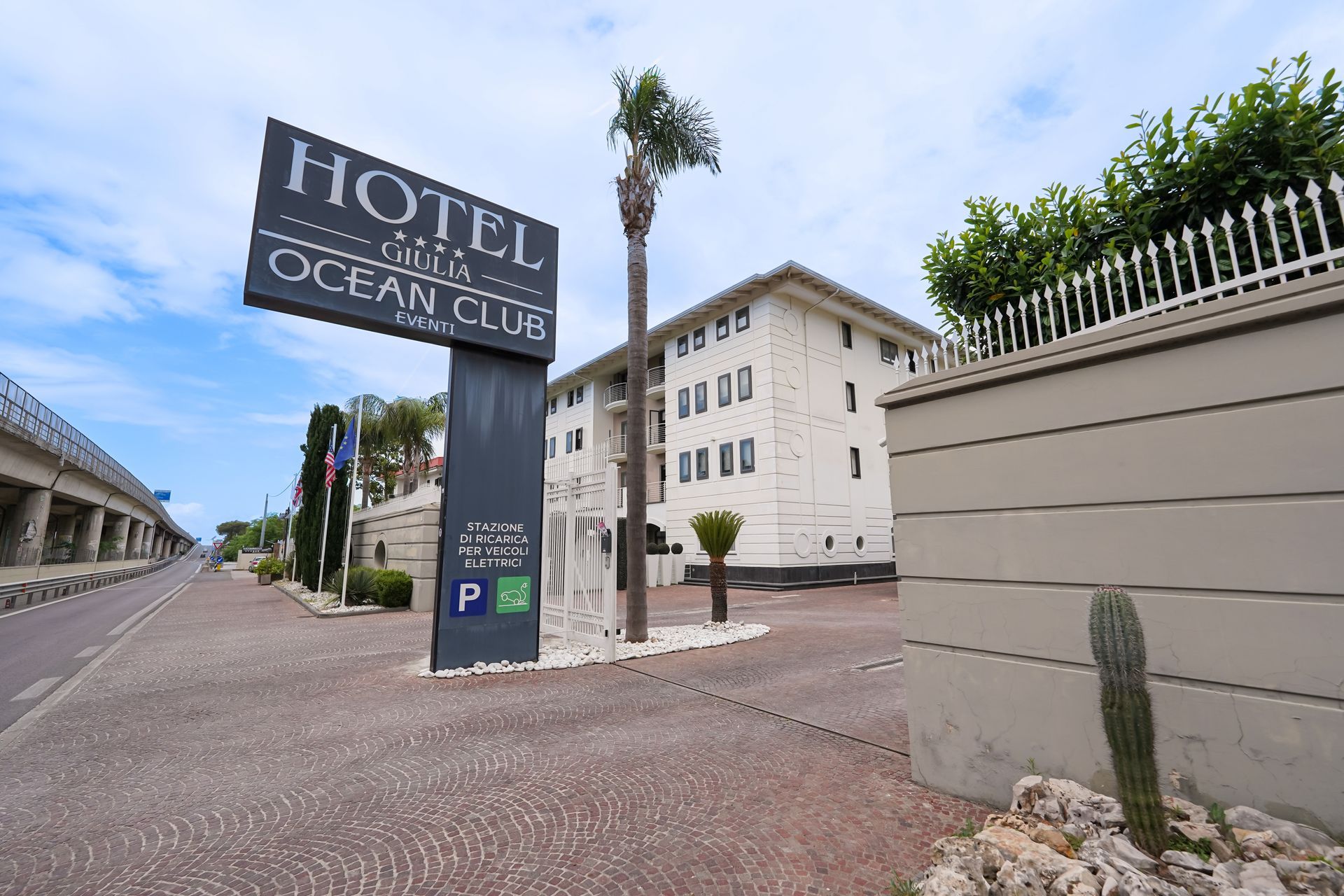 Insegna dell'Hotel Ocean City accanto a un edificio bianco dell'hotel e al parcheggio, con un cactus in primo piano.