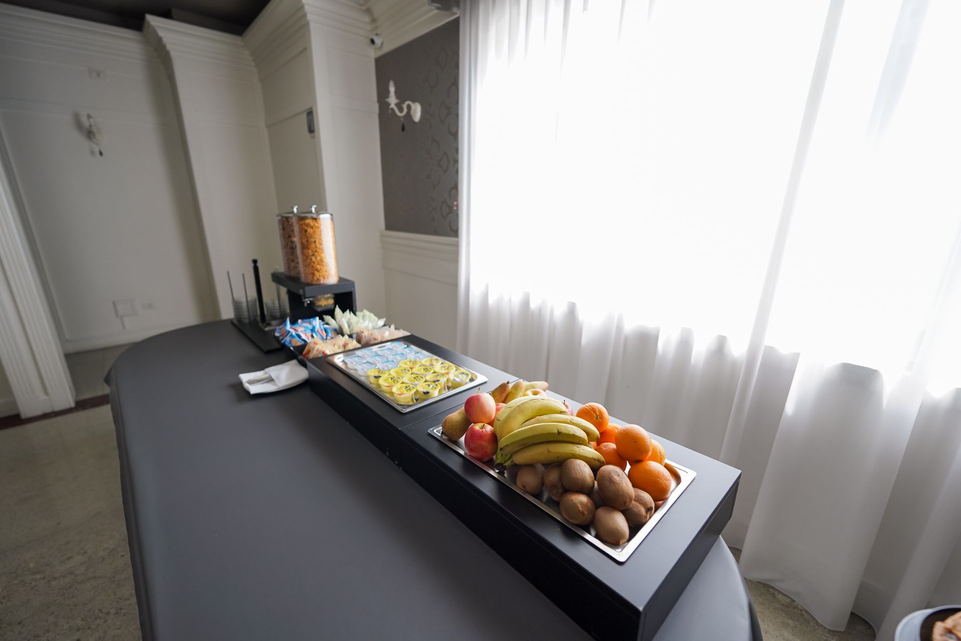 Tavolo da buffet per banchetti con pasticcini, frutta e snack accanto a una finestra luminosa