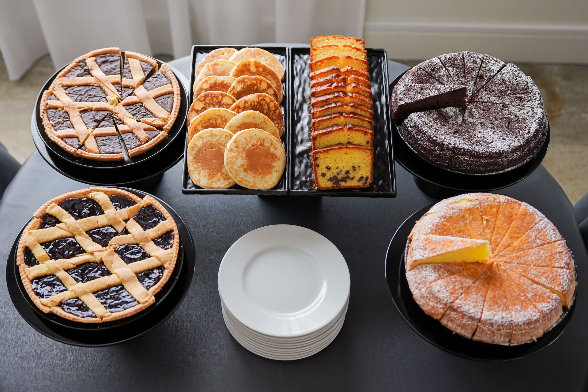 Un assortimento di pasticcini e torte disposti su un vassoio, tra cui crostate a griglia, fette di torta all'arancia e una crostata al cioccolato.
