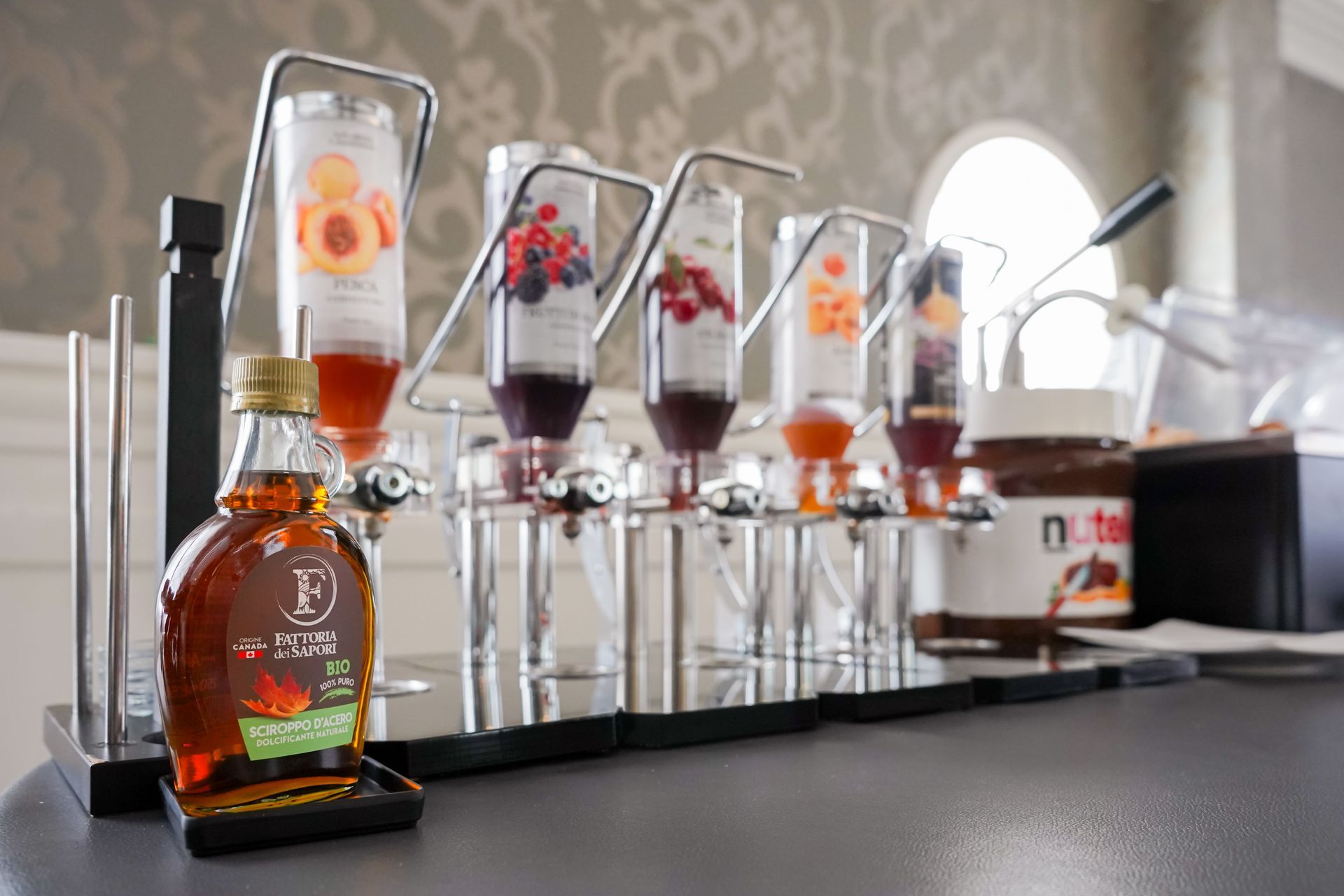 Alti bicchieri da cocktail con bevande a strati sul bancone del bar, accanto a una bottiglia di whisky e a dei dispenser a pompa.