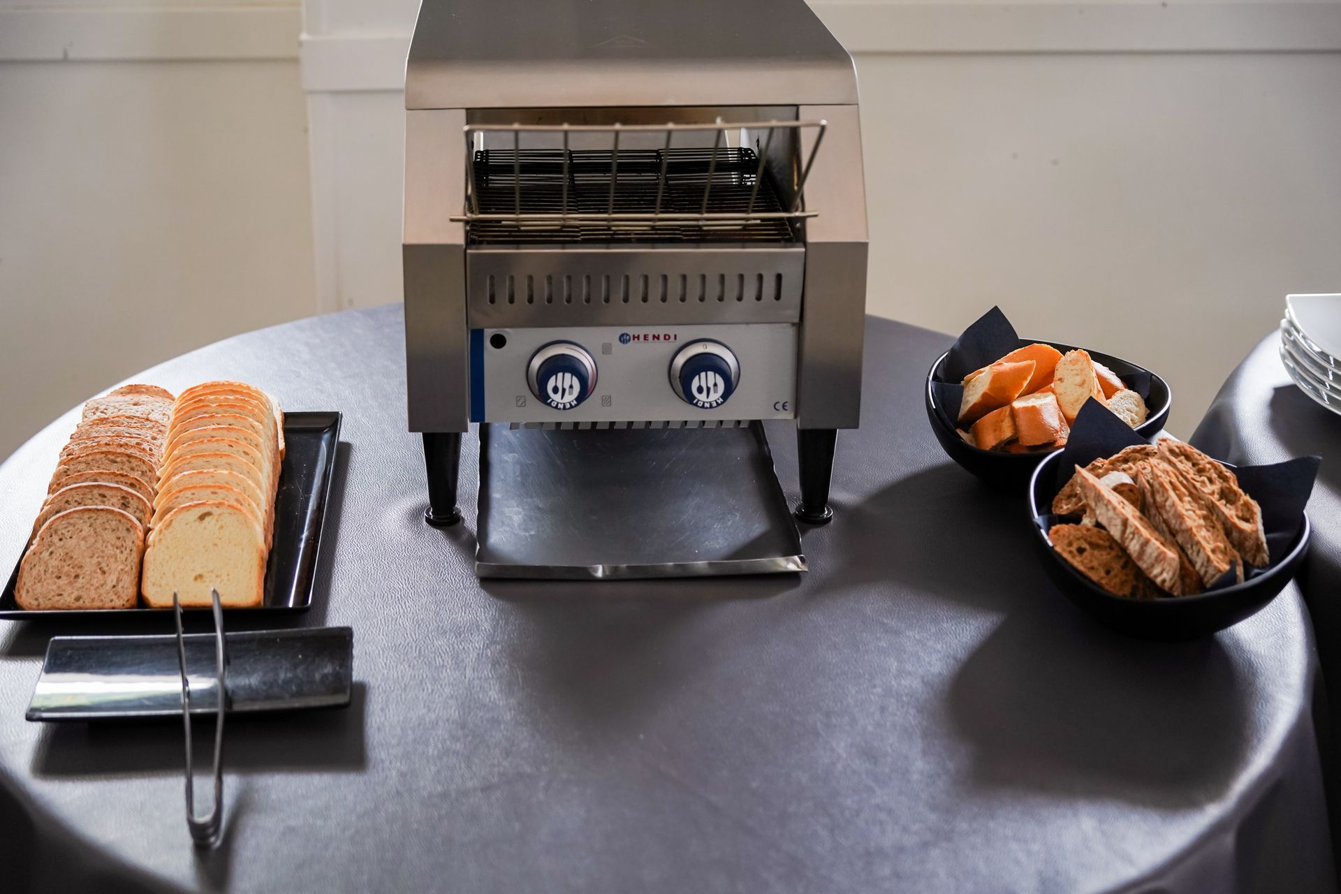 Un tostapane da banco cuoce pane e pasticcini su un tavolo con vassoi di toast e snack.