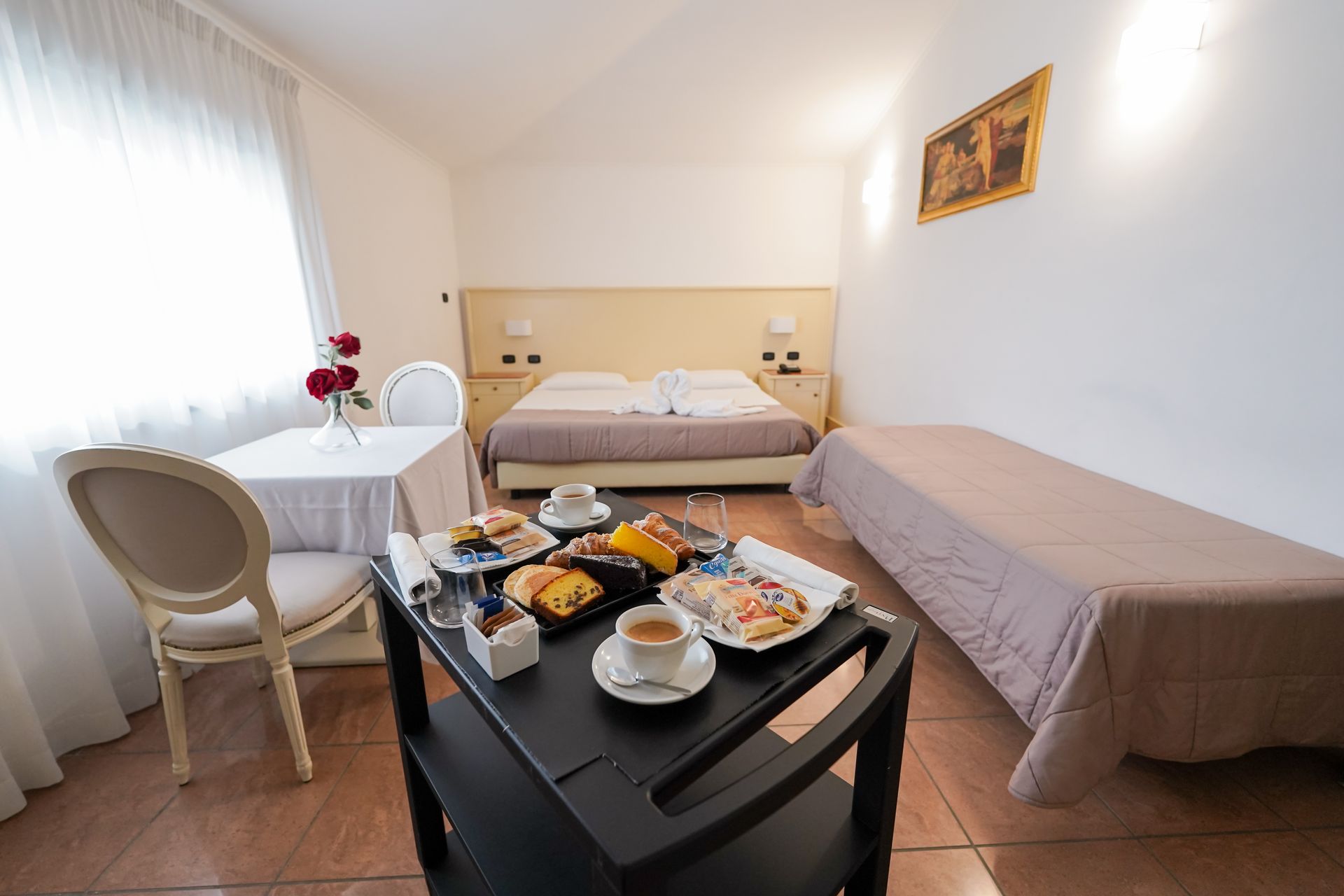 Piccola camera d'albergo con letto, divano, tavolo apparecchiato per la colazione e una finestra luminosa