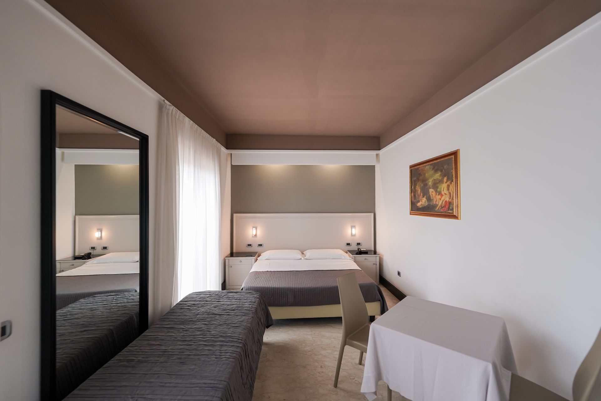 Camera da letto moderna con letto, specchio, finestra e quadro incorniciato alle pareti.