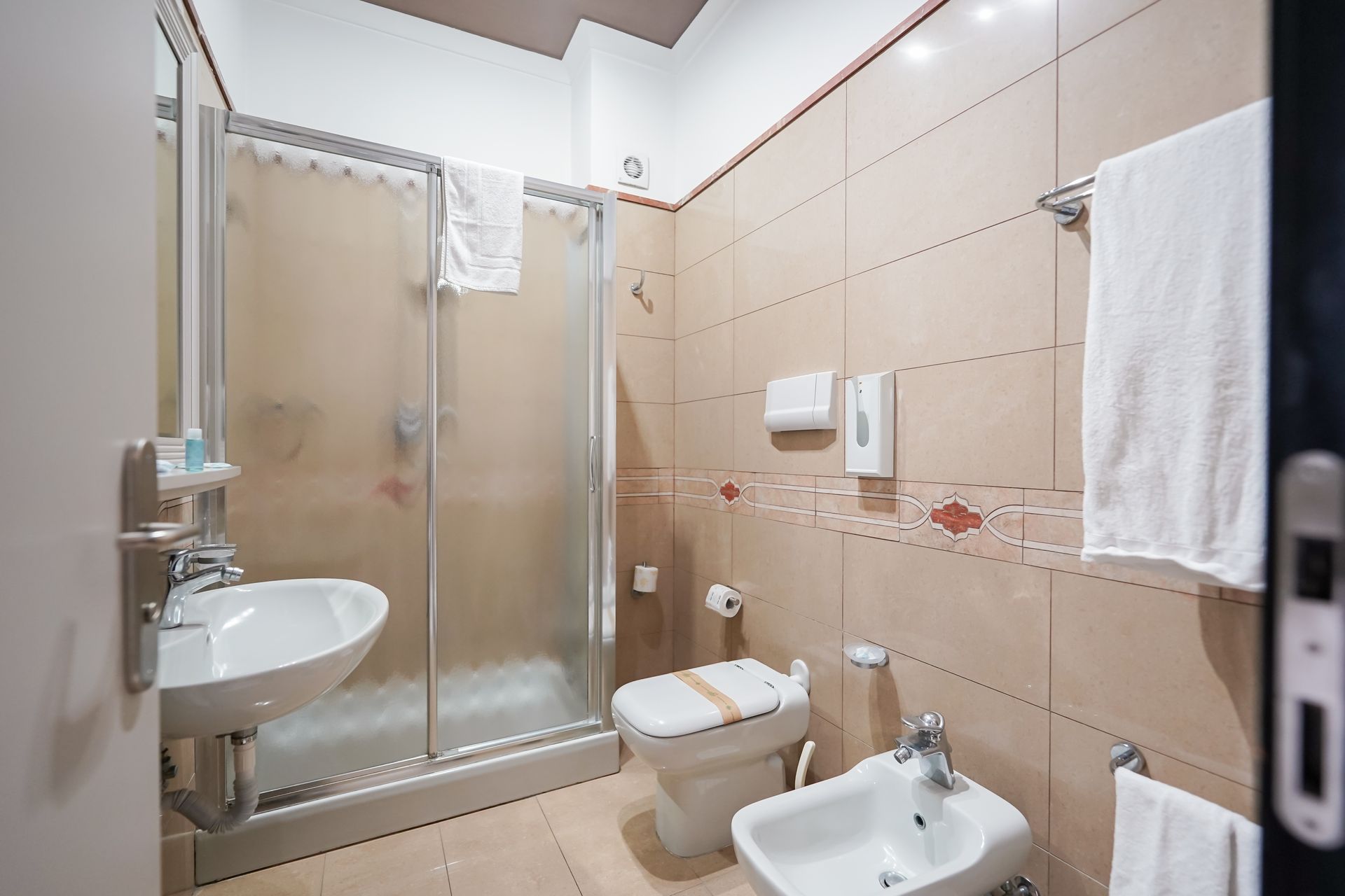 Piccolo bagno piastrellato con box doccia, WC e bidet, oltre ad asciugamani appesi alla parete.