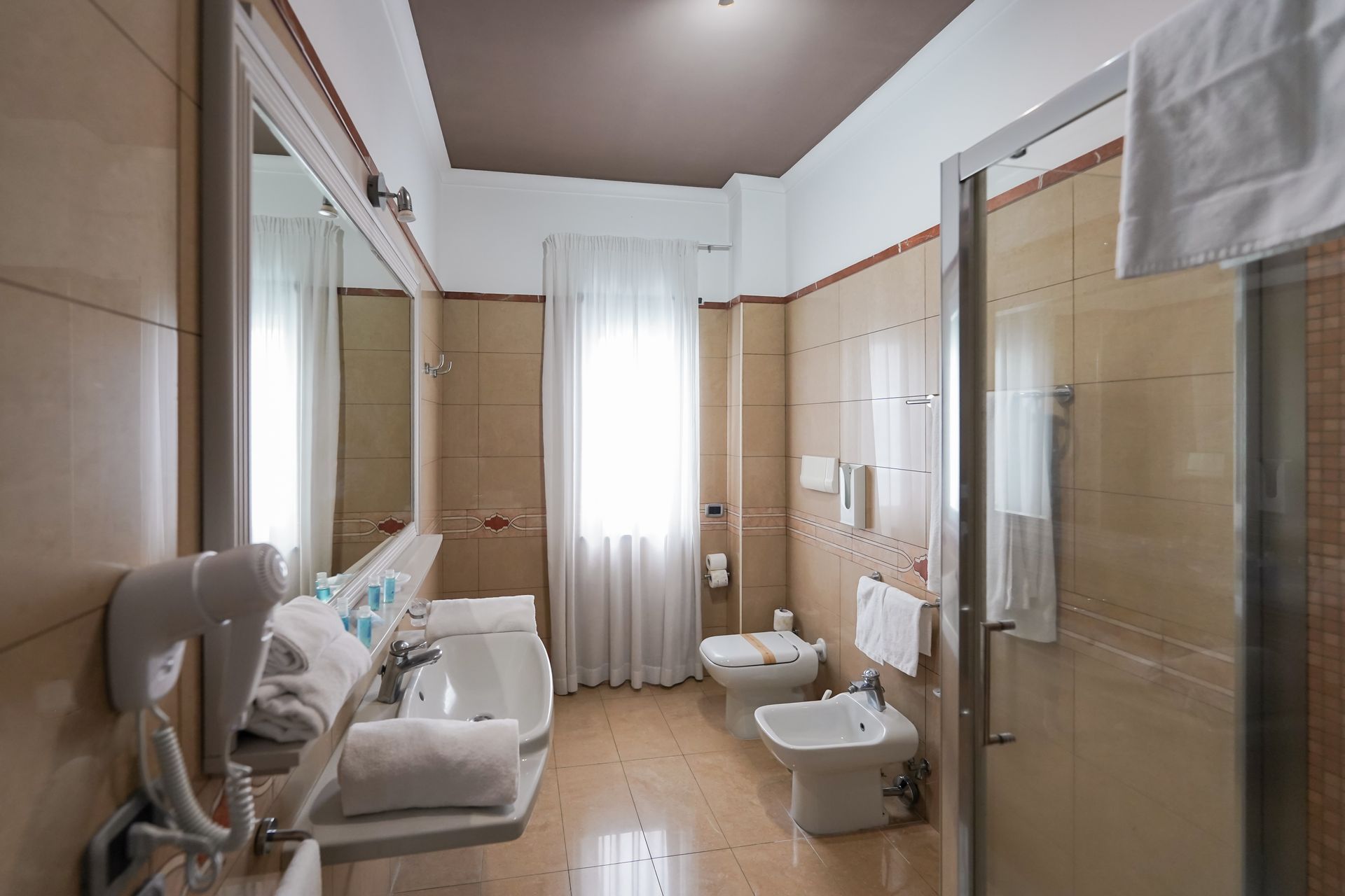 Bagno luminoso con vasca da bagno, lavabo, WC, doccia in vetro e un piccolo divano accanto alla finestra.