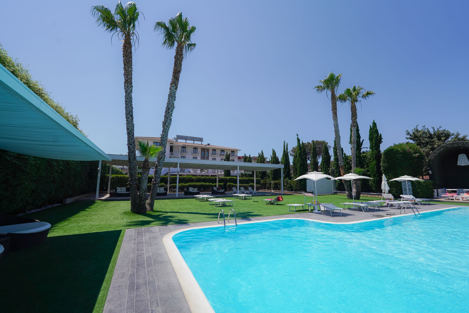 Piscina del resort con acqua turchese, palme, lettini e un edificio alberghiero sullo sfondo.