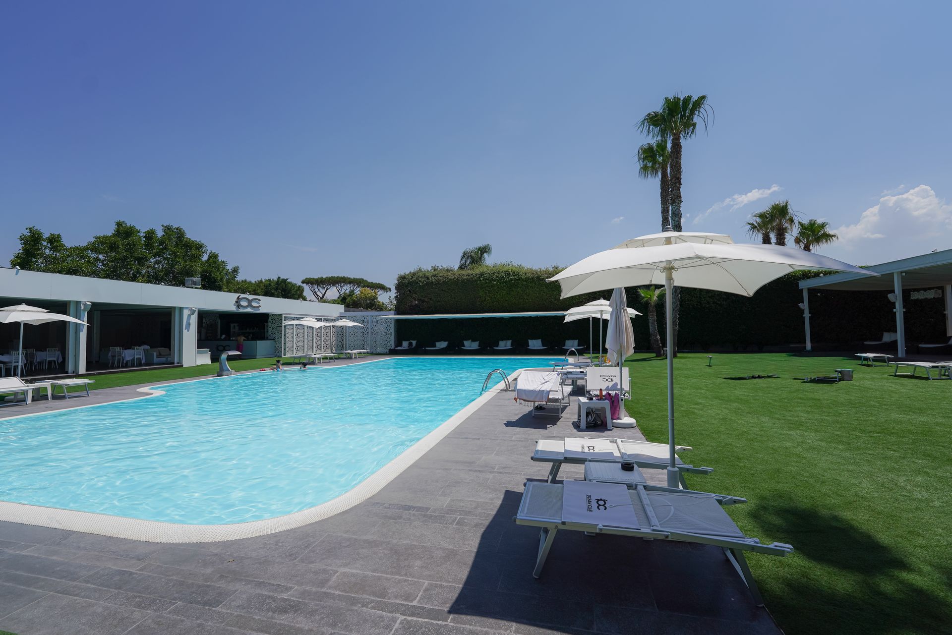 Piscina all'aperto con lettini, ombrelloni e un prato verde sotto un cielo limpido