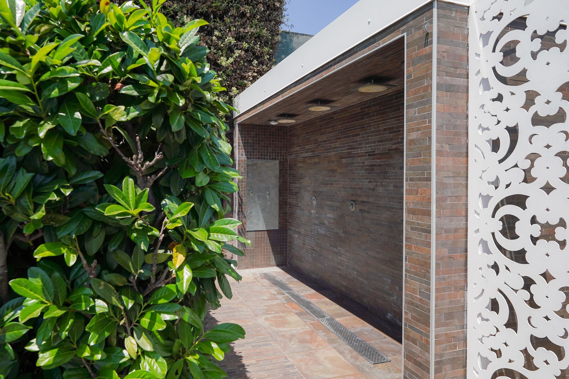 Ingresso di una casa moderna con parete bianca decorata, colonne in mattoni e una rigogliosa siepe verde sulla sinistra.