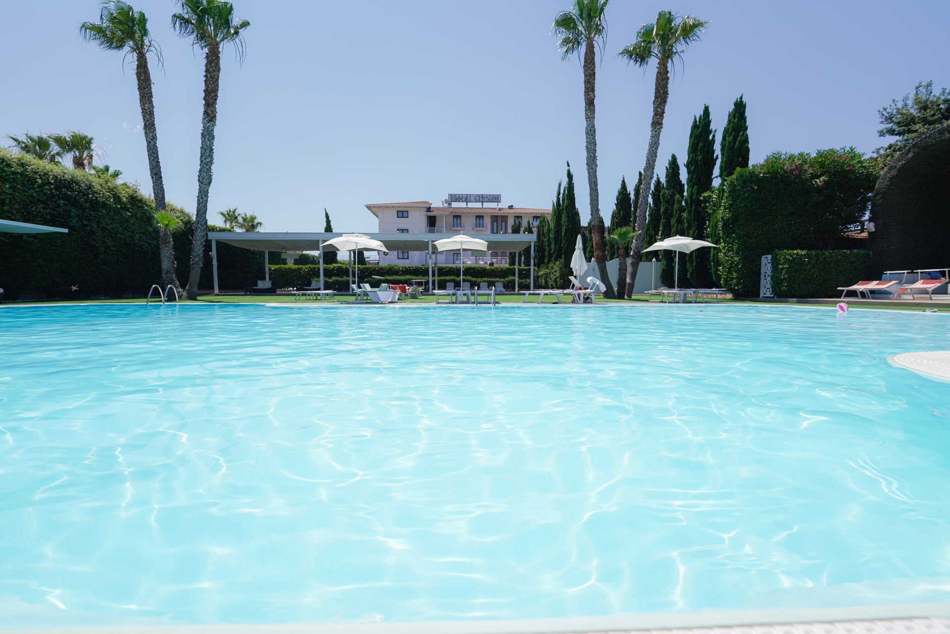 Piscina all'aperto con acqua turchese, palme e un edificio del resort sullo sfondo.