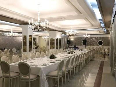 Elegante sala per banchetti con lunghi tavoli drappeggiati di bianco, lampadari e pareti a specchio.