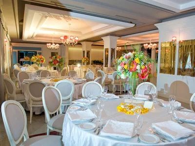 Elegante sala per banchetti con tavoli rotondi, sedie bianche e centrotavola floreali colorati sotto luci calde.