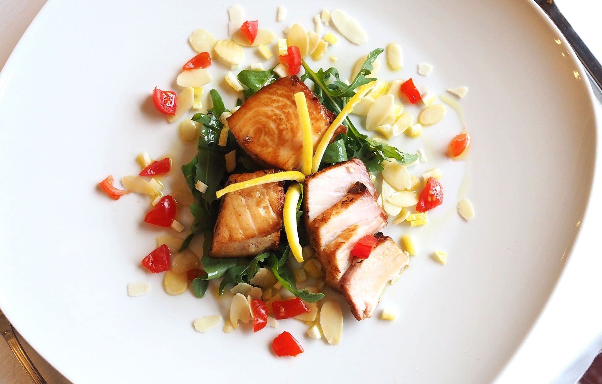 Piatto gourmet impiattato con pesce scottato, verdure e salsa su un piatto bianco.