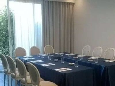 Sala conferenze con un lungo tavolo, tovaglia blu e sedie accanto a una finestra luminosa e tende.