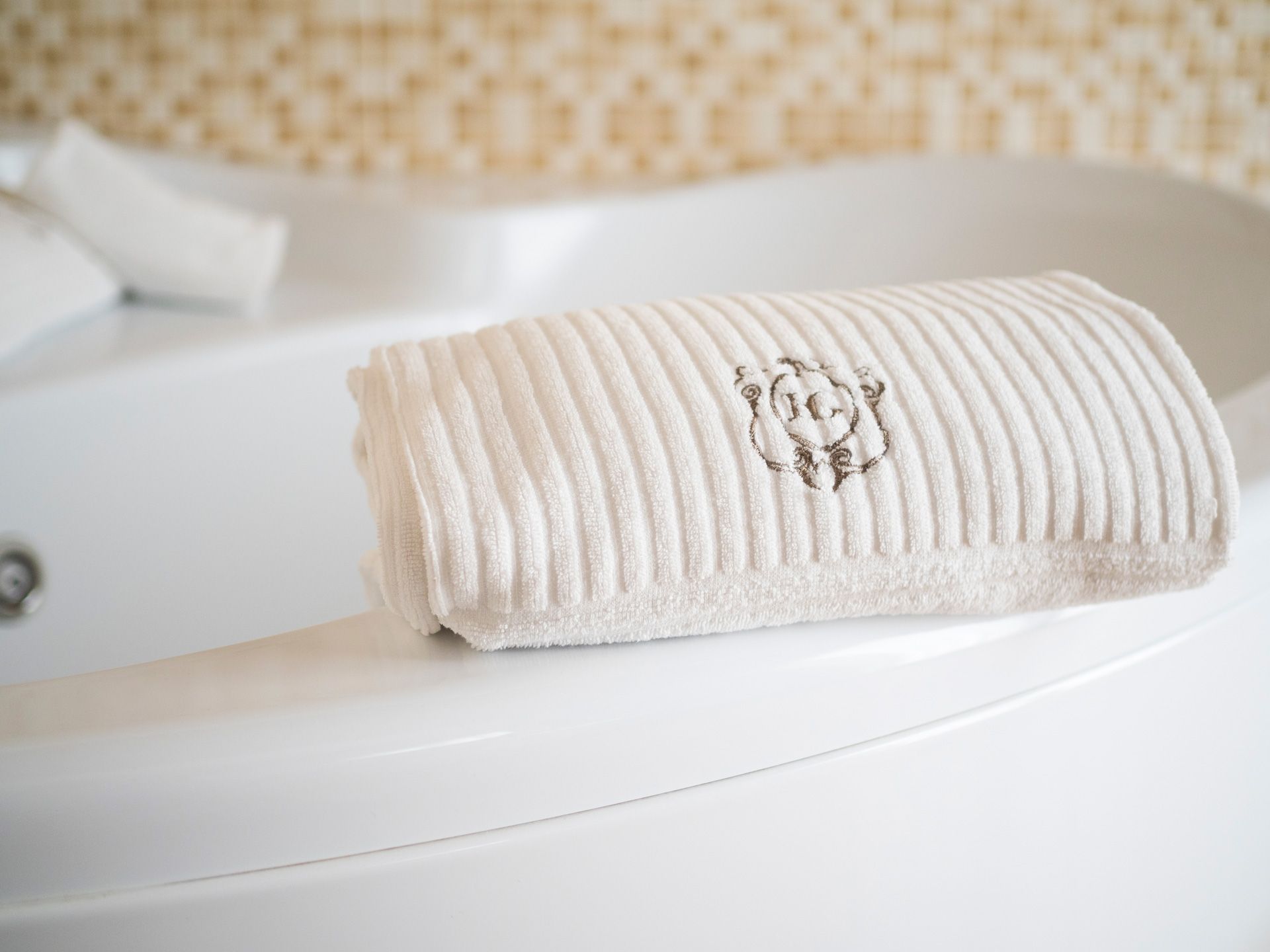Asciugamano bianco a coste arrotolato sul bordo di una vasca da bagno con un emblema argentato