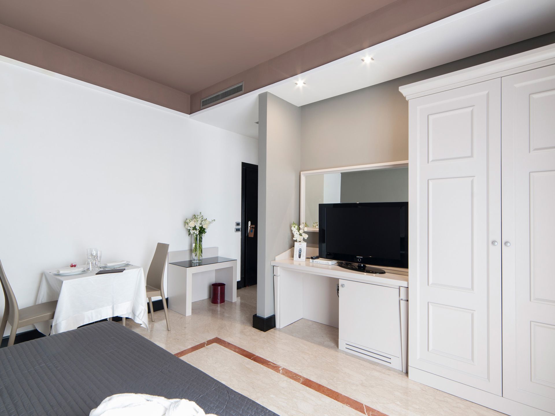 Camera da letto luminosa con armadio bianco, TV, scrivania e un piccolo tavolo da pranzo vicino alla finestra.