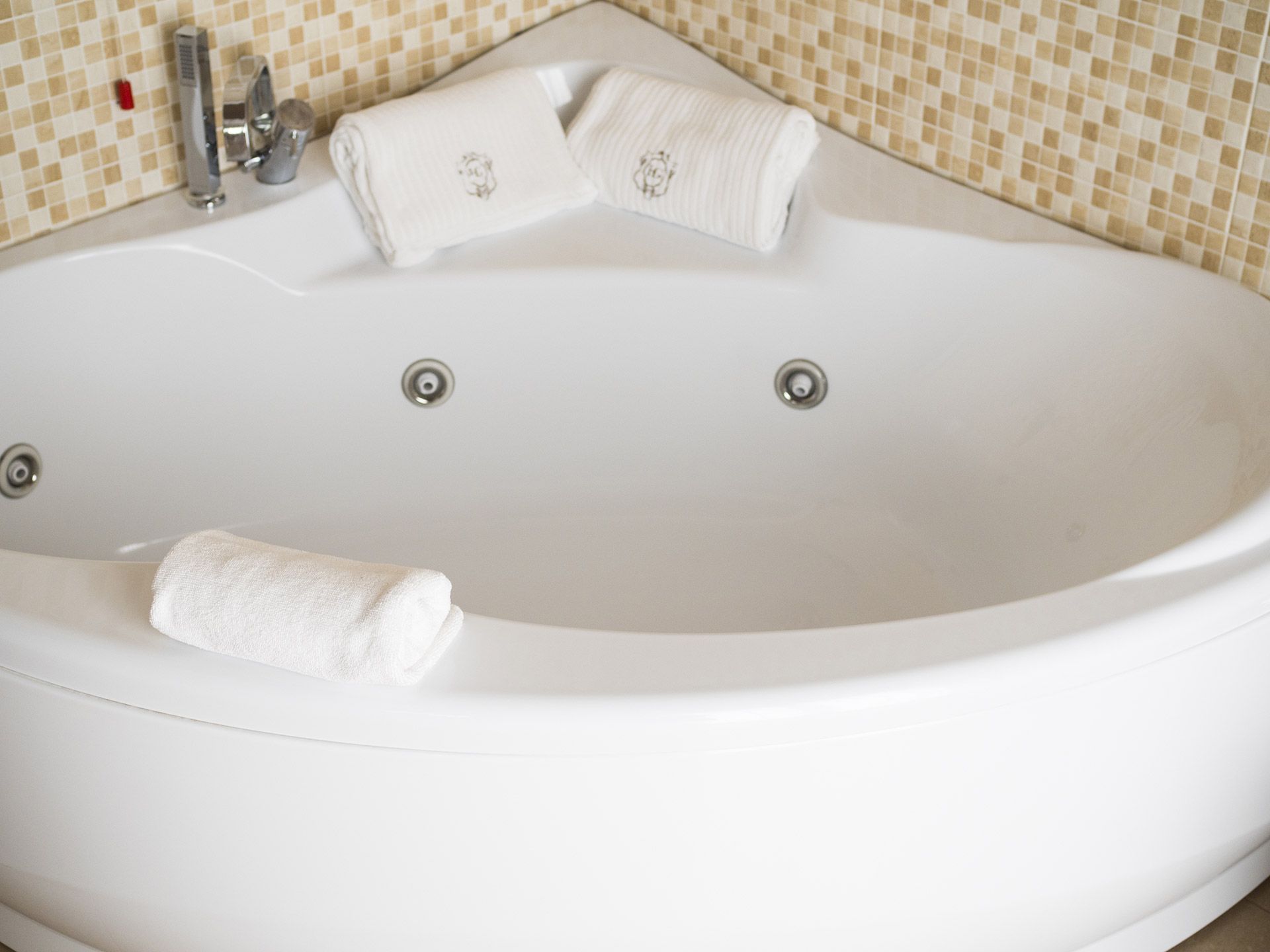 Vasca da bagno ovale bianca con rivestimento in piastrelle a mosaico beige e asciugamani arrotolati sul bordo.
