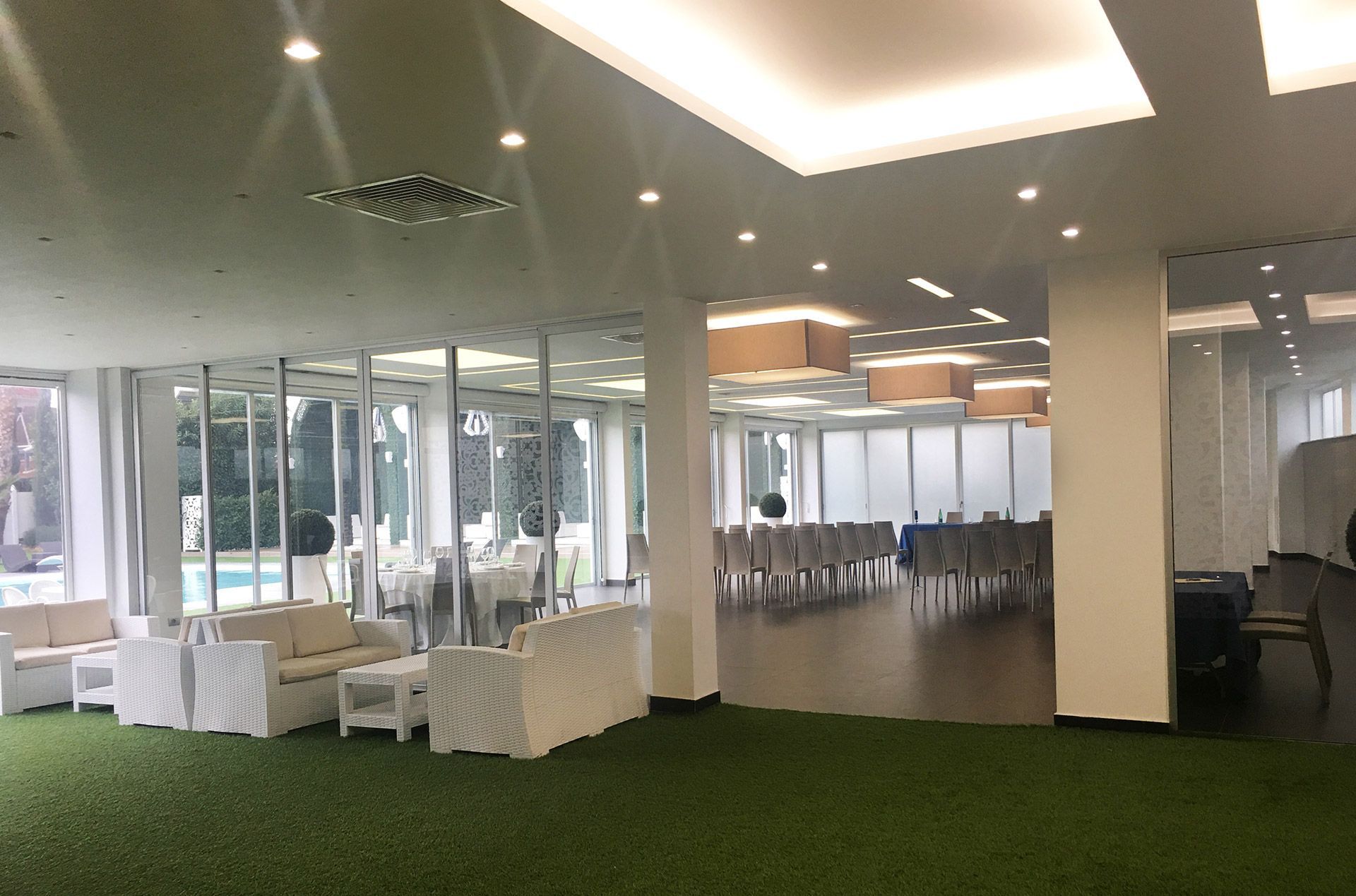 Ampia e moderna sala per banchetti con tavoli apparecchiati con drappeggi bianchi, moquette verde e grandi pareti in vetro.