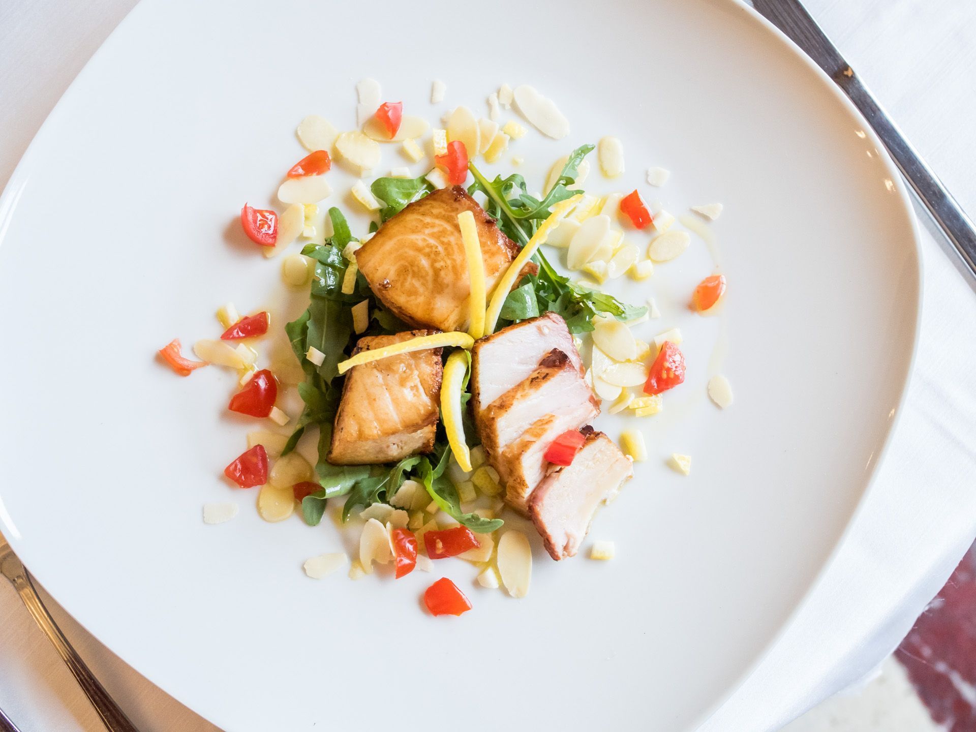 Piatto gourmet di pesce con verdure a dadini e salsa, servito su un piatto bianco.