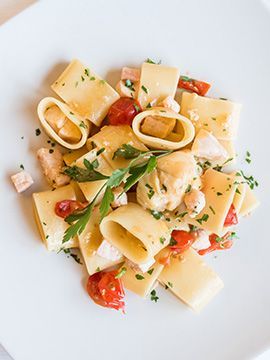 Insalata di pasta con pomodori, erbe aromatiche e scaglie di formaggio su un piatto bianco.