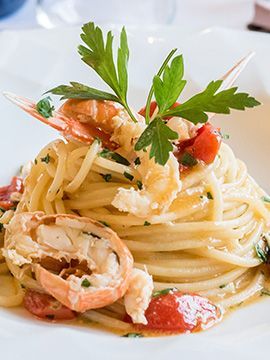 Pasta con gamberi, pomodorini e prezzemolo, servita su un piatto bianco.