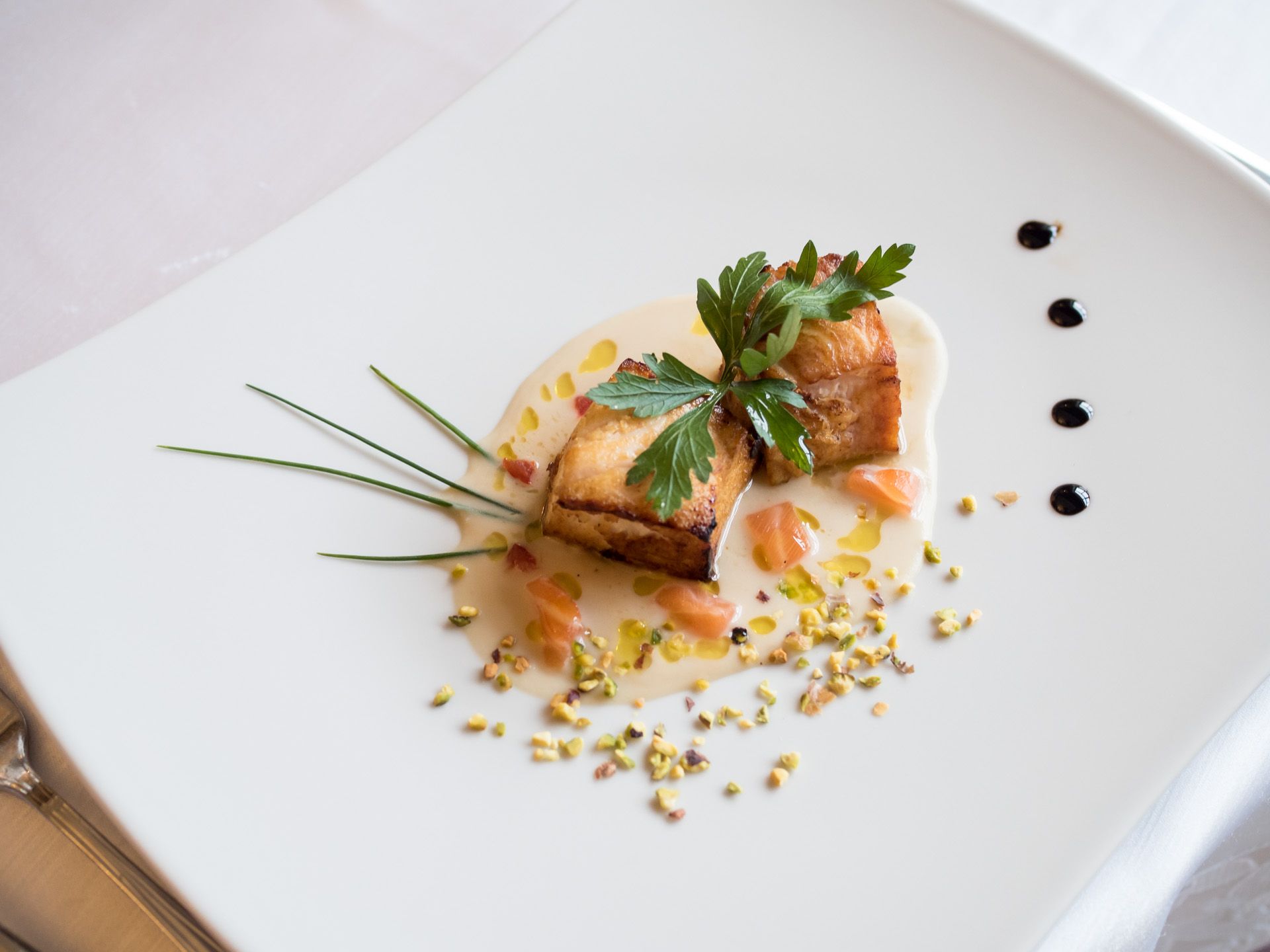 Elegante antipasto servito su un piatto bianco con pesce scottato, guarnizione e gocce di salsa.