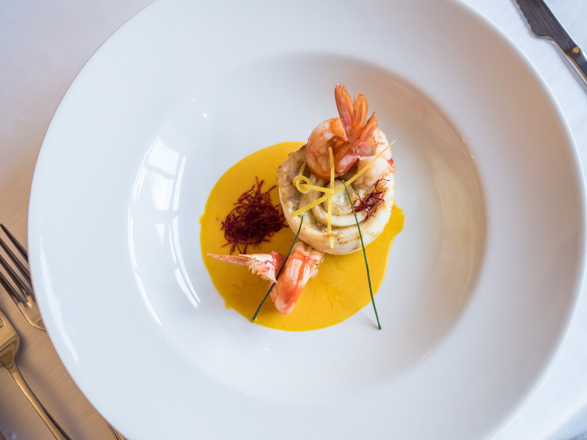 Piatto gourmet impiattato con gamberi, pasta e salsa gialla su un piatto bianco.