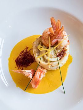 Piatto di gamberi con salsa giallo brillante, guarnizione di zafferano e microverdure su un piatto bianco.