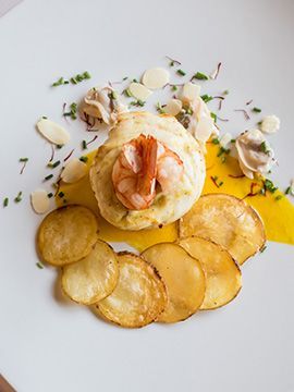 Piatto gourmet impiattato con bignè alla crema guarnito con gamberetti, patatine fritte e salsa gialla su un piatto bianco.