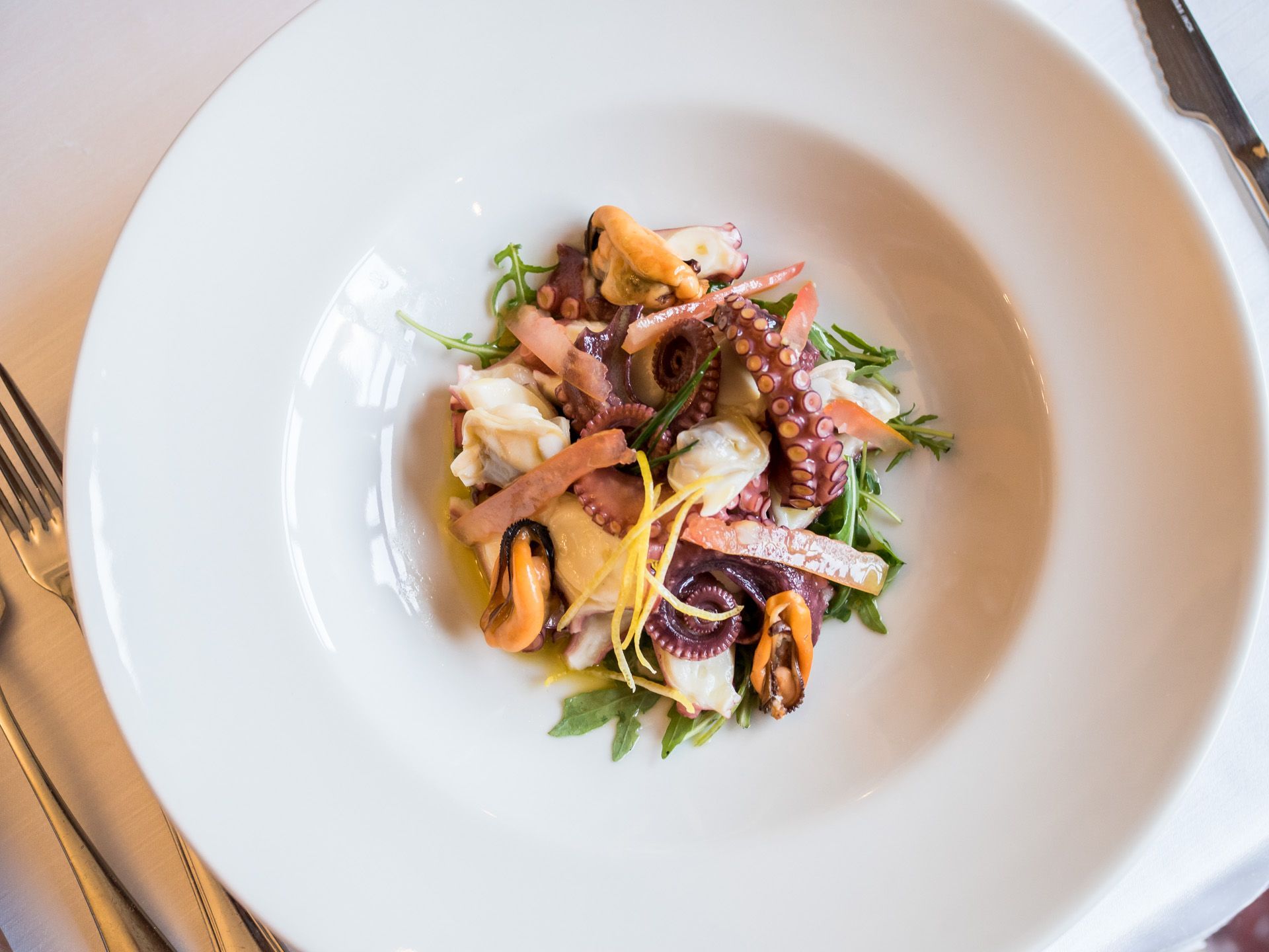 Piatto di frutti di mare con cozze, calamari e verdure, servito su una tavola bianca.