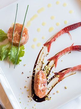 Piatto di gamberi impiattato con salsa, verdure e guarnizione decorativa su un piatto bianco.