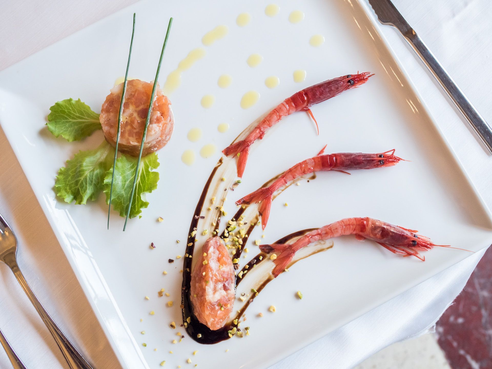 Piatto gourmet di pesce con gamberi, verdure e salsa, servito su un piatto bianco.