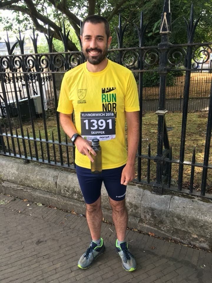 Man in yellow shirt with race bib, holding water bottle, smiling outdoors.