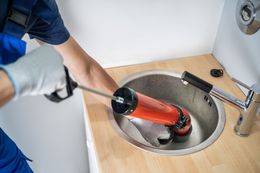 Plumber using a drain auger to unclog a sink in a bathroom or utility room