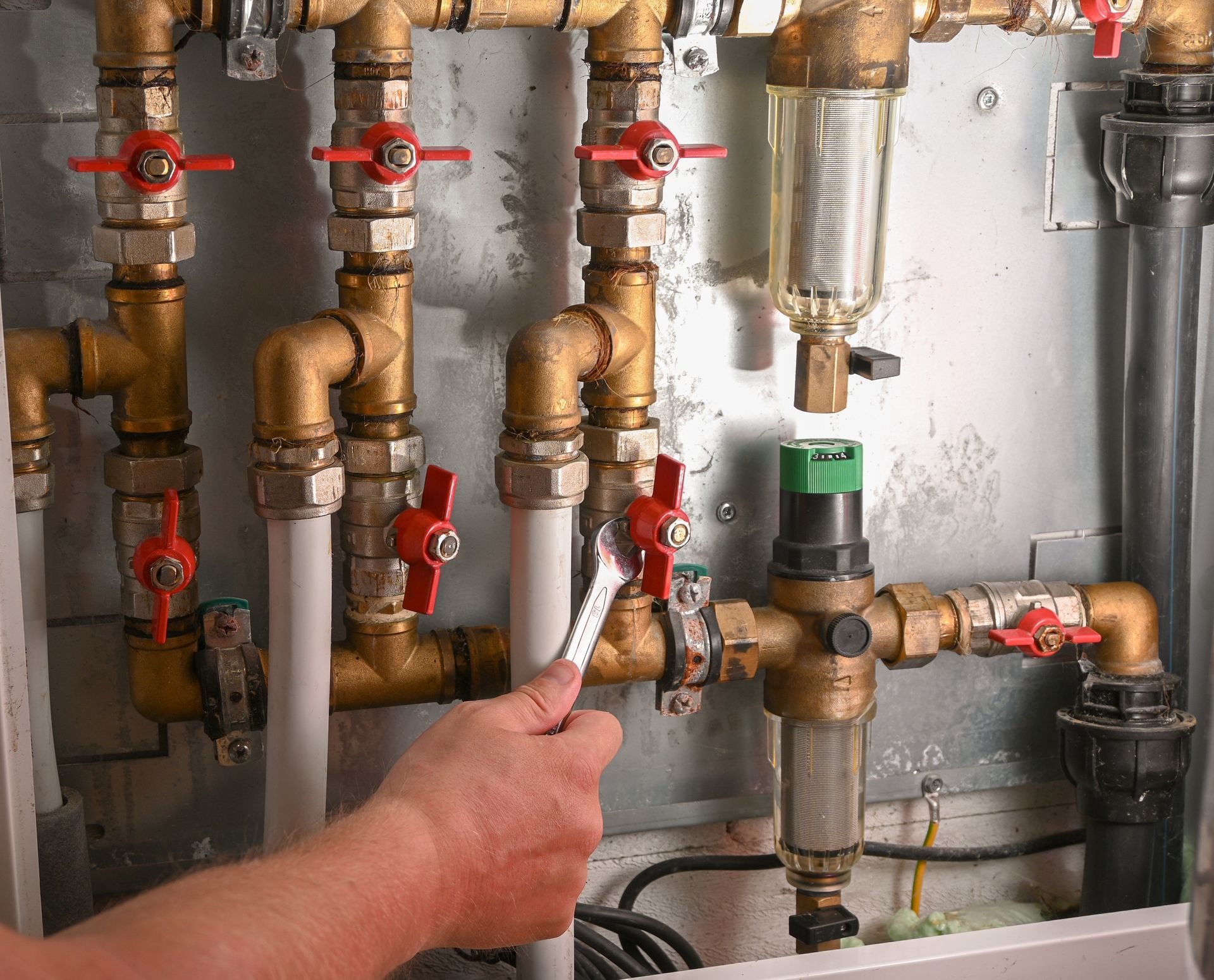 Technician adjusting a valve on industrial pipes with red handles and a pressure gauge in a utility room