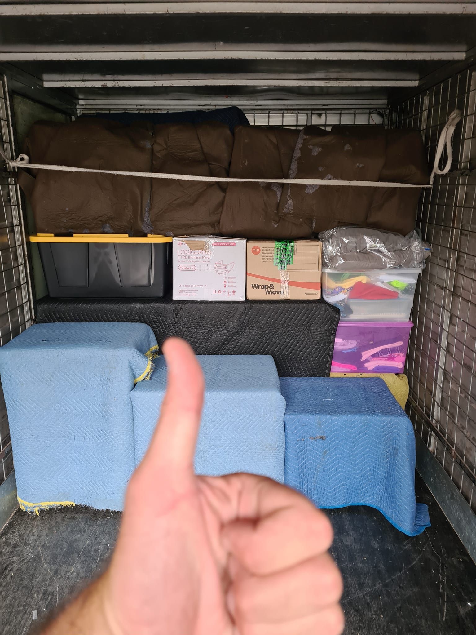 Inside a Van, a Thumb-Up in Front of Stacked Boxes, Bins, and Blue-Covered Items — MM Removals In Nelson Bay, NSW